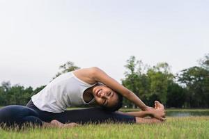 ung asiatisk kvinna yoga utomhus behåll lugnet och mediterar medan du utövar yoga för att utforska den inre friden. yoga har goda fördelar för hälsan nära sjön i parken. sport och hälsosam livsstil koncept. foto