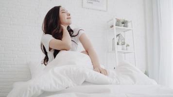 vacker asiatisk kvinna som sträcker ut sin kropp efter att hon vaknat i sitt sovrum hemma. glad kvinna njuta av solig morgon. livsstil kvinna hemma koncept.