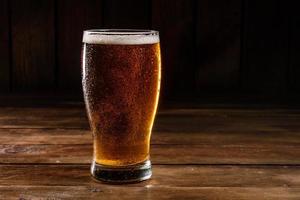 glas ljus öl på en mörk pub foto