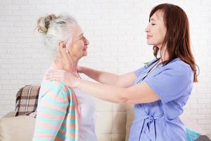 kvinnlig kiropraktor tittar på äldre kvinna med nacksmärta på läkarmottagningen eller hemmet foto