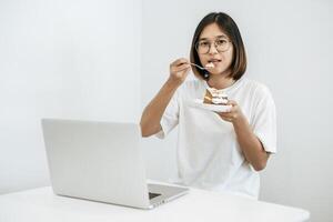 flickan äter tårta och har en bärbar dator på bordet. foto