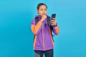 porträtt av eftertänksam asiatisk ung man tittar på mobiltelefon på blå bakgrund foto