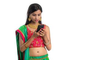 ung indisk traditionell flicka som använder en mobiltelefon eller smartphone isolerad på en vit bakgrund foto