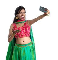 vacker ung glad tjej som tar en selfie med lerlampa eller diya under festivalen av ljus diwali med en smartphone på en vit bakgrund foto