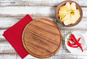 kryddig röd chili potatischips och tom bräda på ett träbord foto