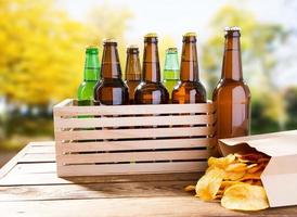 ölflaskor och packa potatischips på träbord på suddig parkbakgrund foto