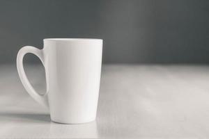 vit keramisk kopp på vitt träbord på grå bakgrund. plats för text eller reklam foto