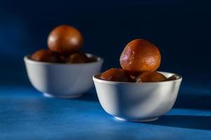 indisk dessert gulab jamun i skål med sked på blå bakgrund foto