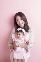 asiatisk mamma och bedårande flicka är glada på rosa bakgrund foto
