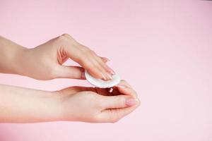 ung kvinna ta bort nagellack på rosa bakgrund. foto