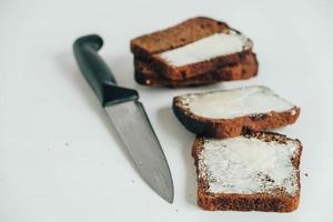 skivat brunt bröd med smör och en kökskniv på en vit träbakgrund foto