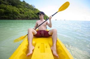 en ung sportig man som paddlar kajak vid havet i en solig dag foto