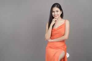 mode porträtt av vacker kvinna som bär orange klänning isolerad över grå bakgrund studio foto