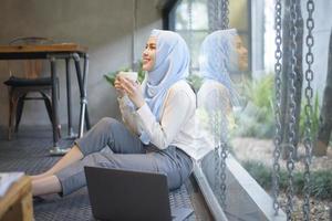 muslimsk kvinna med hijab arbetar med bärbar dator i kaféet
