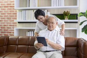 ett lyckligt senior asiatiskt par använder surfplatta och pratar med familjen på webbkameran hemma, pensionskoncept.