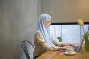 muslimsk kvinna med hijab arbetar med bärbar dator i kaféet
