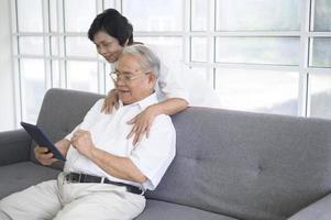ett lyckligt senior asiatiskt par använder surfplatta och pratar med familjen på webbkameran hemma, pensionskoncept. foto