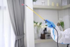 en medicinsk personal i ppe-kostym använder desinfektionsspray i vardagsrummet, covid-19-skydd, desinfektionskoncept. foto