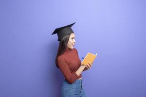 porträtt av ung universitetsstudent kvinna med examen mössa på violett bakgrund foto