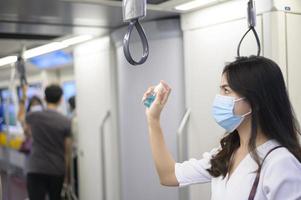 en ung kvinna som bär skyddsmask i tunnelbanan använder alkohol för att tvätta händerna, resa under covid-19-pandemin, säkerhetsresor, socialt avståndsprotokoll, nytt normalt resekoncept foto