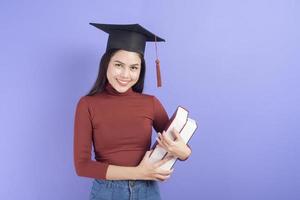 porträtt av ung universitetsstudent kvinna med examen mössa på violett bakgrund foto