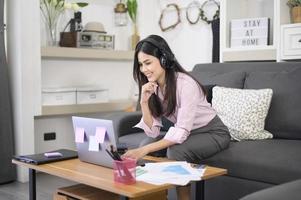 en vacker ung kvinna som bär headset ringer videokonferenssamtal via datorn hemma, affärsteknologiskt koncept. foto