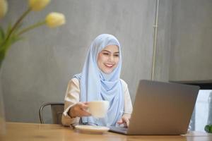 muslimsk kvinna med hijab arbetar med bärbar dator i kaféet foto