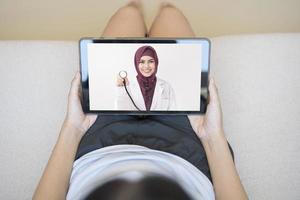 surfplatta övervaka över flickans axel, en muslimsk läkare kvinna bär uniform och ger konsultation till unga kvinnor, sjukvårdsteknologikoncept