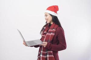 ung leende kvinna bär röd jultomte hatt ringer videosamtal på sociala nätverk med familj och vänner på vit bakgrund studio. foto