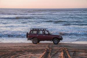 röd offroad bil parkerad vid kusten på sanden på stranden på kvällen foto