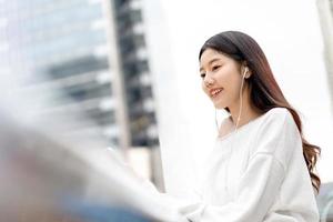 ung söt asiatisk tjej lyssnar på musik i hörlurar i staden foto