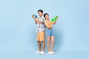 Ungt asiatiskt par i sommardräkter med vattenpistoler i studio blå bakgrund för songkran festival i Thailand och Sydostasien foto