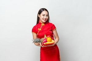 ung asiatisk kvinna i traditionell röd cheongsam-klänning som håller lyckliga frukter för kinesiskt nyår i ljusgrå isolerad studiobakgrund foto