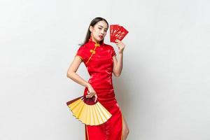 asiatisk kvinna i orientalisk cheongsam-dräkt som håller röda kuvert eller ang pao och fläkt på ljusgrå studiobakgrund för kinesiska nyårskoncept, text betyder stor lycka stor vinst foto