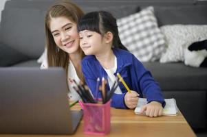 asiatisk glad mamma och dotter använder laptop för att studera online via internet hemma. e-lärande koncept under karantän. foto