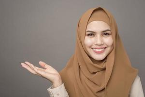 porträtt av vacker kvinna med hijab visar något på hennes hand på grå bakgrund foto