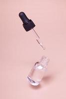 flytande droppflaska i glas med serum eller olja och en flygande pipett. hudvård minimalistisk koncept mock up foto