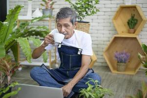 glad senior asiatisk pensionerad man med bärbar dator kopplar av och njuter av fritidsaktivitet i trädgården hemma. foto