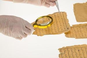 en forskare studerar arabisk skrift från Koranen med hjälp av ett förstoringsglas och ett bord med ljus. paleografi, studiet av forntida arabisk skrift foto