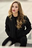 vacker ung flicka som bär svart jacka sitter på gatan. foto