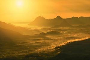 underbart landskap soluppgång berg med dimma dimma gul guld himmel och stigande solsken på morgonen på kullen foto