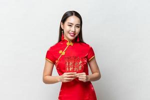 leende glad asiatisk kvinna i traditionell orientalisk kostym håller röda kuvert eller ang pao i ljusgrå bakgrund för kinesiska nyårskoncept, text betyder stor lycka stor vinst foto