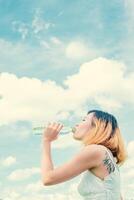 kvinnor livsstil koncept ung vacker kvinna med vit klänning dricksvatten på sommaren grön park. foto