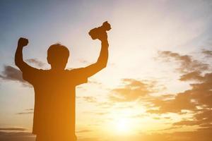 siluett av en ung man som håller kameran, sträck ut armarna medan solnedgången. foto