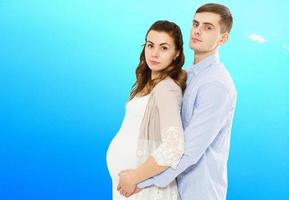 porträtt av ungt par i väntan på barnet isolerat på blå bakgrund, ungt attraktivt par gravid mamma och lycklig pappa, vackert ungt par som väntar barn foto