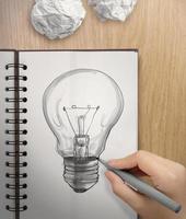 hand med en penna ritning glödlampa på anteckningsbok som koncept foto
