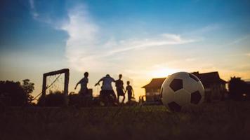 siluett actionsport utomhus av barn som har roligt att spela fotboll för träning i samhällets landsbygdsområde under skymningens solnedgångshimlen foto