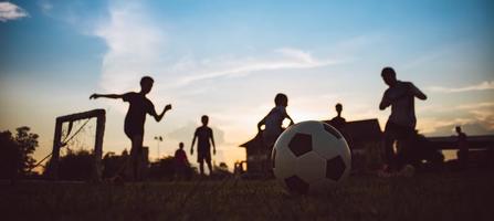 siluett actionsport utomhus av barn som har roligt att spela fotboll för träning i samhällets landsbygdsområde under skymningens solnedgångshimlen foto