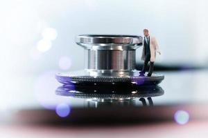 modern medicinsk koncept-studio makro av miniatyr läkare med ett stetoskop och digital surfplatta på trä bord bakgrund foto