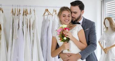 älskare ger blommor till bruden och kysste glada och par älskar stående i bröllop studio foto